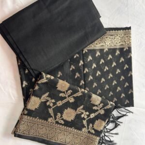 A black Chanderi Suit featuring gold floral and leaf patterns is neatly folded on a white surface. The set includes a matching black blouse piece and a dupatta (pallu) adorned with gold designs and tassels, highlighting the elegance of Chanderi fabric.