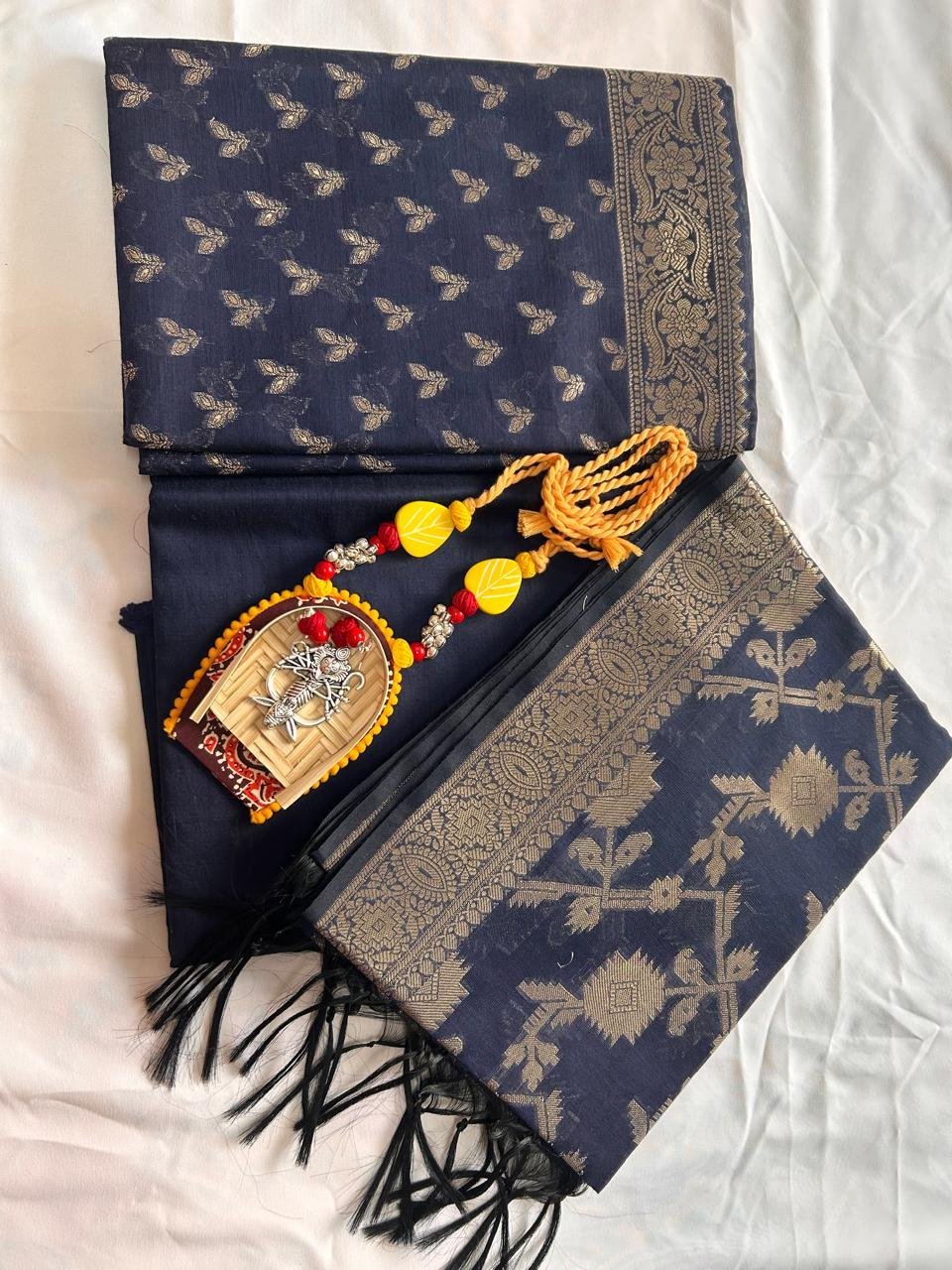 A folded Chanderi Suit in navy blue and gold with intricate patterns, paired with a decorative Hindu necklace featuring a small image of Lord Krishna, displayed on a white background.