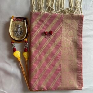 A folded pink and gold Banarasi Silk Dupatta with tassels, accompanied by a small decorative wooden ornament adorned with red and yellow beads, and two red earrings, all arranged on a white surface.